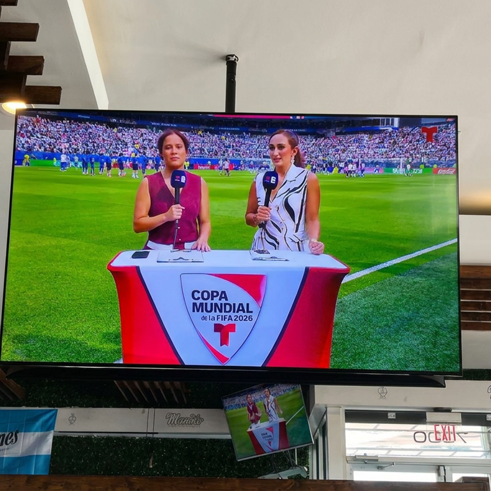 Restaurant interior with Argentine flags and televisions showing two presenters broadcasting from a FIFA World Cup soccer field.